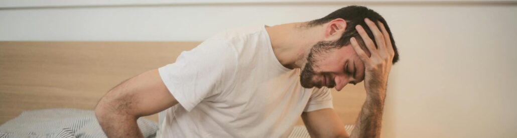 a man sitting on a bed and holding his head in his hand